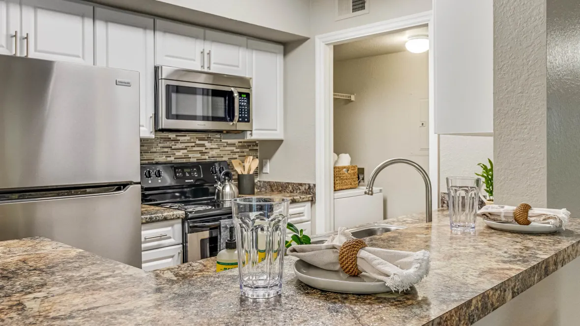 Peering from the living room across the open granite-inspired breakfast bar into the kitchen, revealing an unobstructed view with an adjacent laundry room.