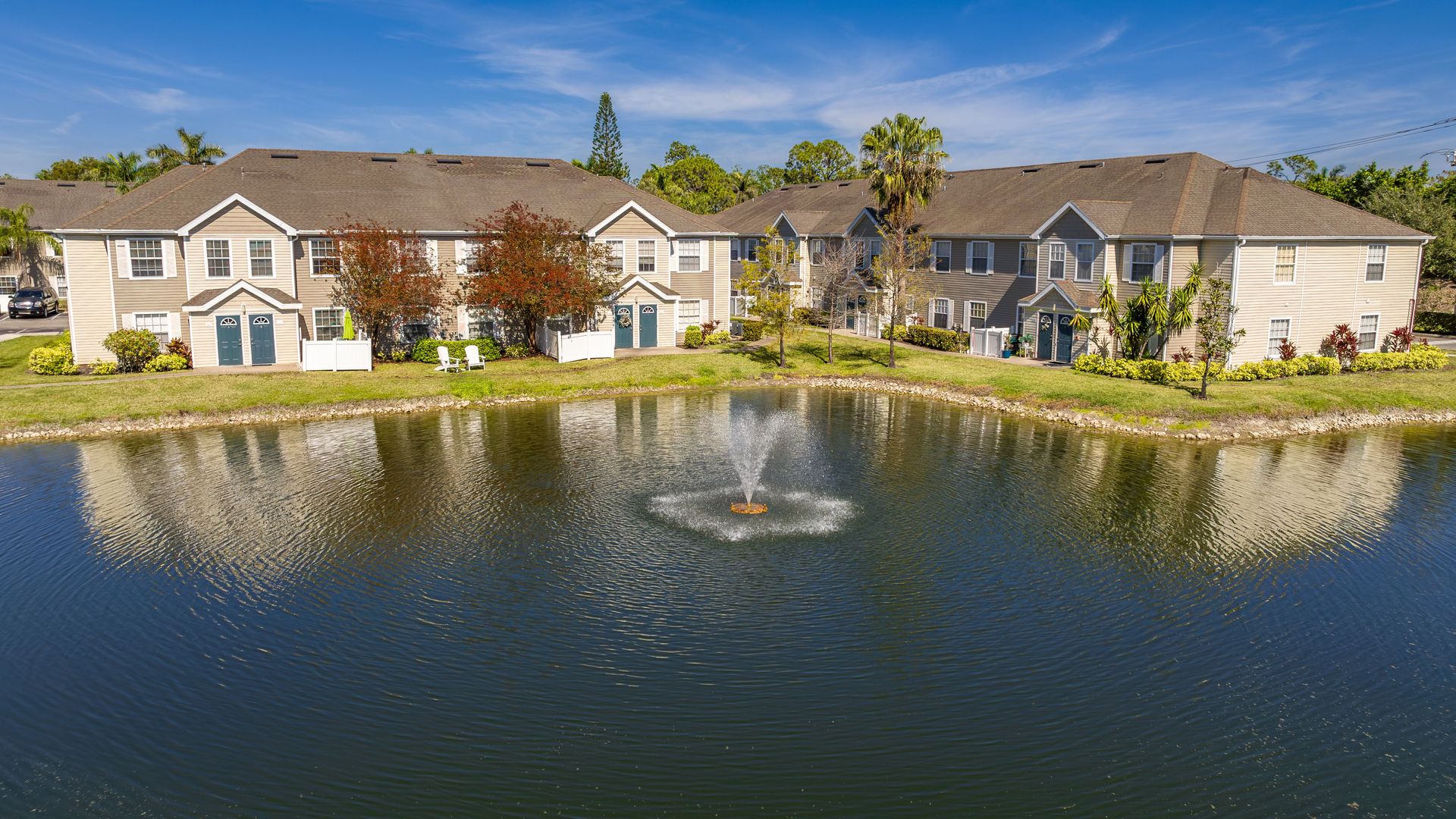 A serene lake with a fountain in the center, surrounded by well-maintained apartment homes and vibrant landscaping.