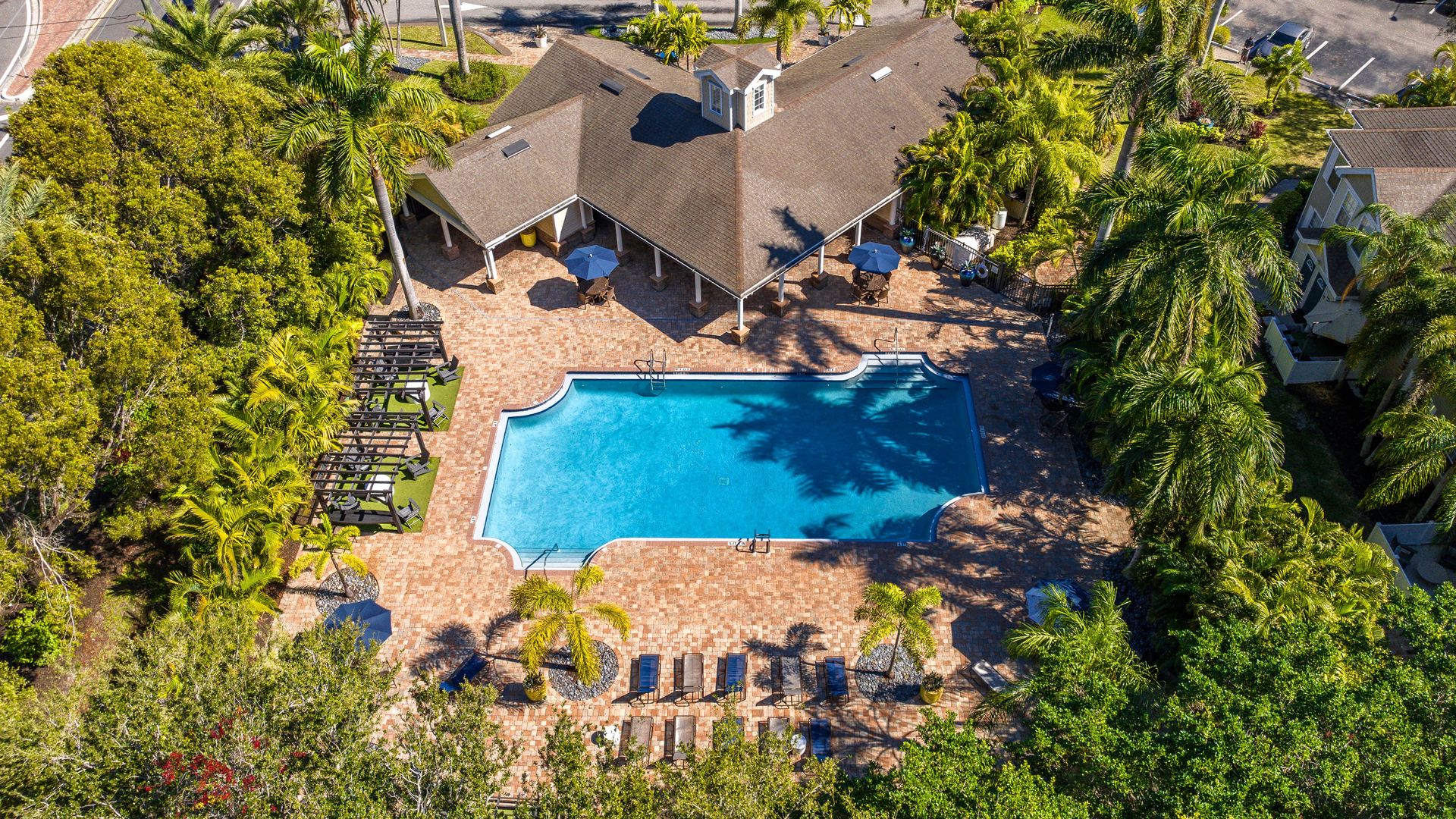 Aerial view of the pool and sundeck at Meadow Lakes Apartments, featuring lounge chairs, pergolas, and tropical landscaping.