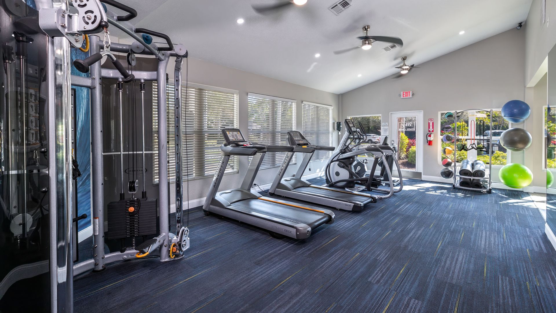 Spacious fitness center at Meadow Lakes with cardio machines, weight training equipment, and large windows bringing in natural light.