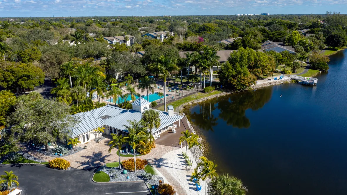 An aerial view of the River Reach community, adorned with lush tropical landscaping, a tranquil lake, and vibrant outdoor amenities including swimming pools and a sandy beach area.