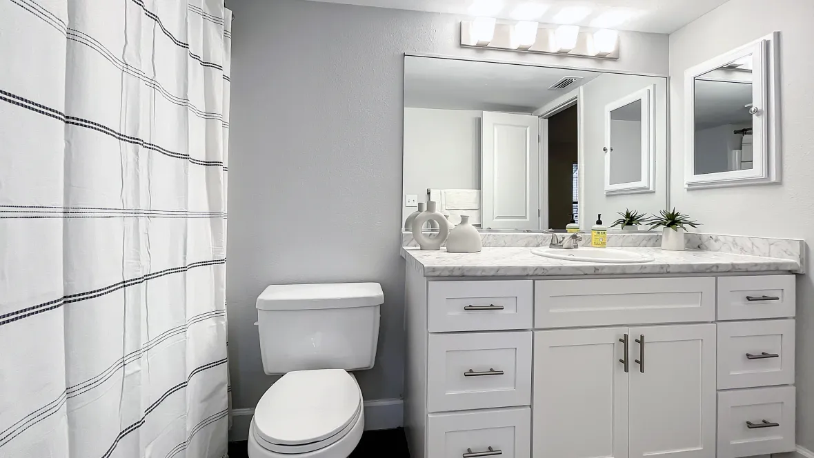  A vibrant bathroom adorned with stunning white cabinets, drawers, and countertops, illuminated by radiant vanity lighting, exuding attractive modernity in every nook and cranny.