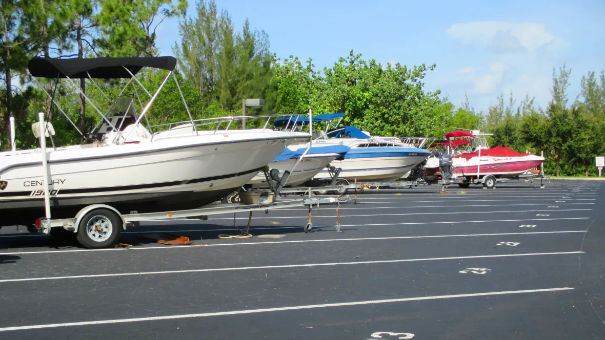 Several boats parked in a large, paved lot with lengthy, huge, numbered spots for assigned parking spots.  Reserved boat parking area, offering residents a secure space to park their boats with access to the Gordon River.