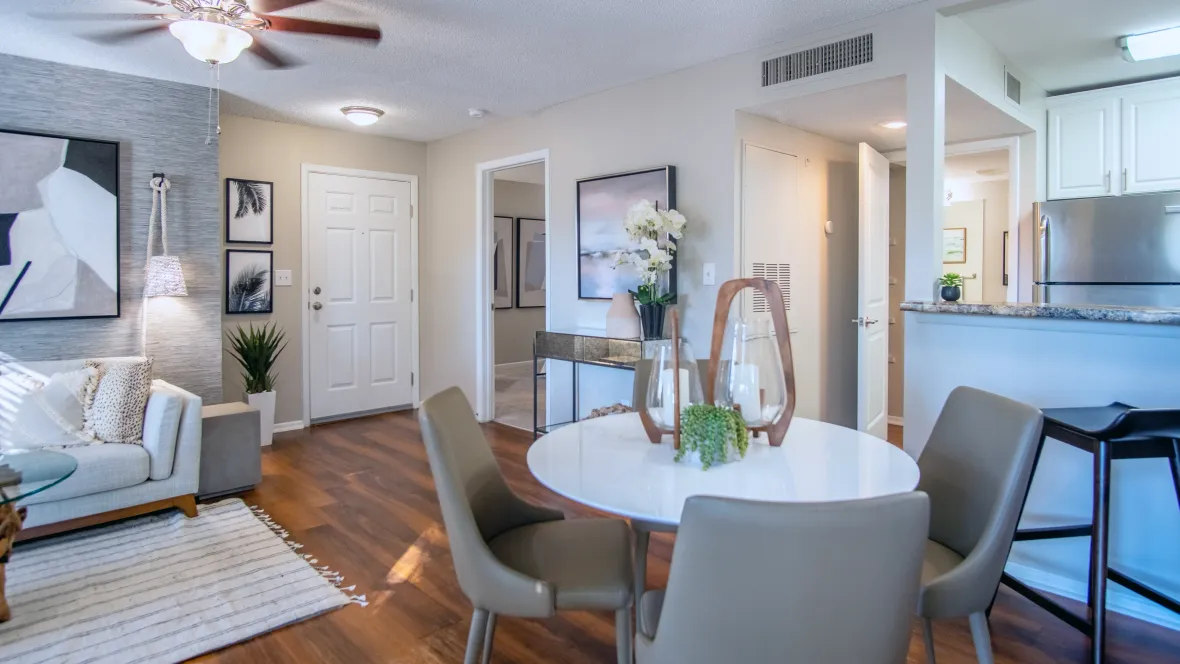 Living and dining rooms with sleek wood-like flooring, illuminated by a ceiling fan, offering a comfortable and stylish space for dining and relaxing at River Reach.