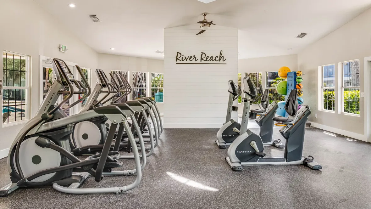 Ellipticals and rowing bikes face a wall of bright open windows, providing inspired workout views directly overlooking the resort-style pool.