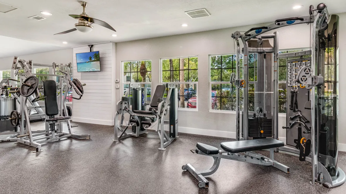 A view of a corner in the weight training room showcasing a bench with a total-body workout system, various weight assisted machines with a sleek gym floor for an ideal space to sculpt and tone. 