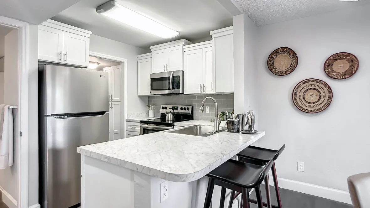 A fully-equipped kitchen featuring modern countertops, brilliant overhead lighting reflecting off stainless-steel appliances, and a breakfast bar with stools.