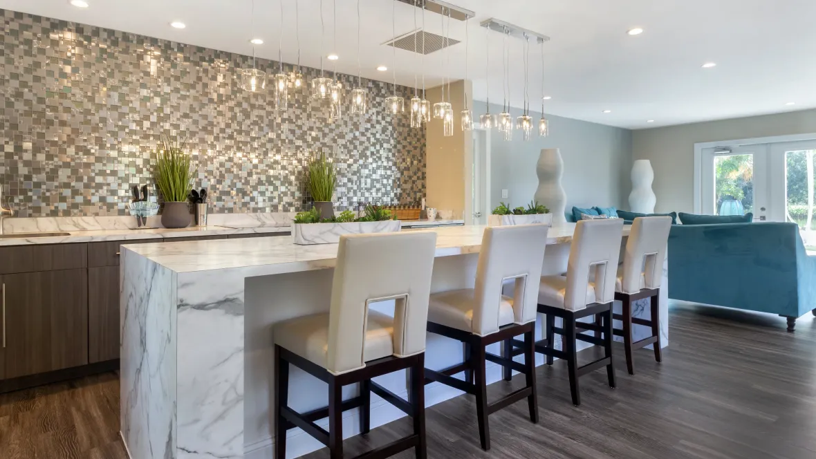 The refined clubroom completed with four sophisticated bar stools, accentuated by graceful pendant lighting above a spacious kitchen island—a perfect setting for mixing beverages, engaging in creative endeavors, or hosting lively gatherings.