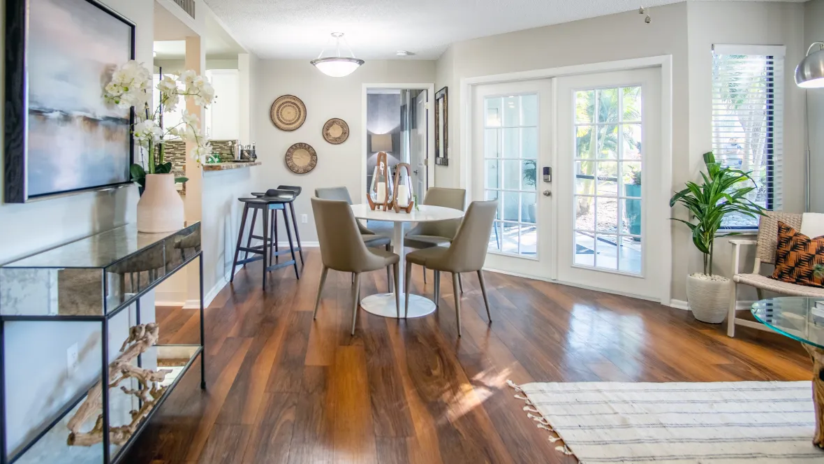 An expansive floor plan showcasing the modern design of a living and dining room space with fluid wood-plank flooring and French-style patio doors, offering a seamless flow.