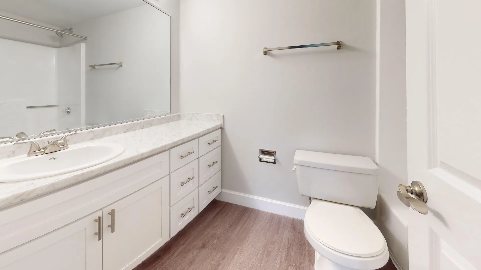 Bathroom in the Martinique floor plan at River Reach, featuring white cabinetry, marble countertops, a large mirror, and light wood flooring.