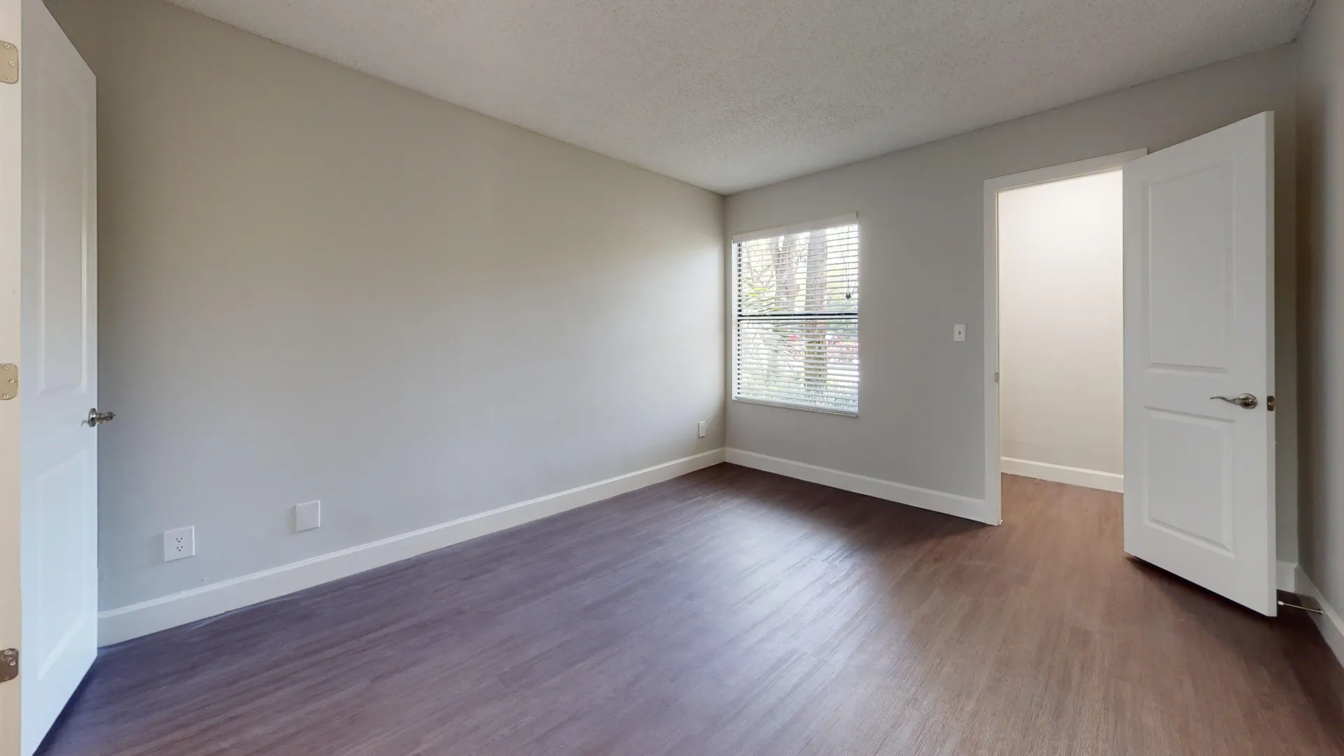 Bedroom in the Martinique floor plan, showcasing large windows, neutral walls, and wood-style flooring.