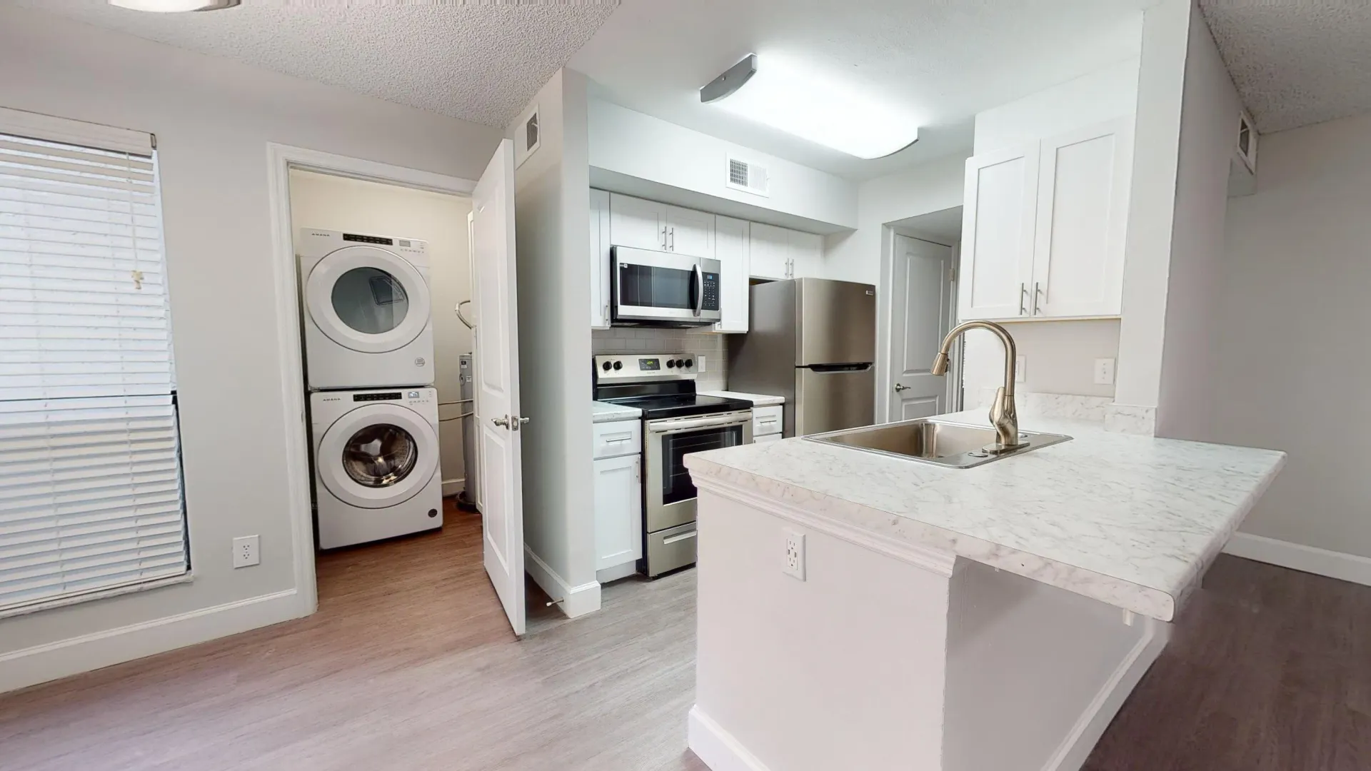 Kitchen and laundry area in the Martinique floor plan, featuring stainless steel appliances, white cabinetry, and a stackable washer and dryer set in a well-lit space.