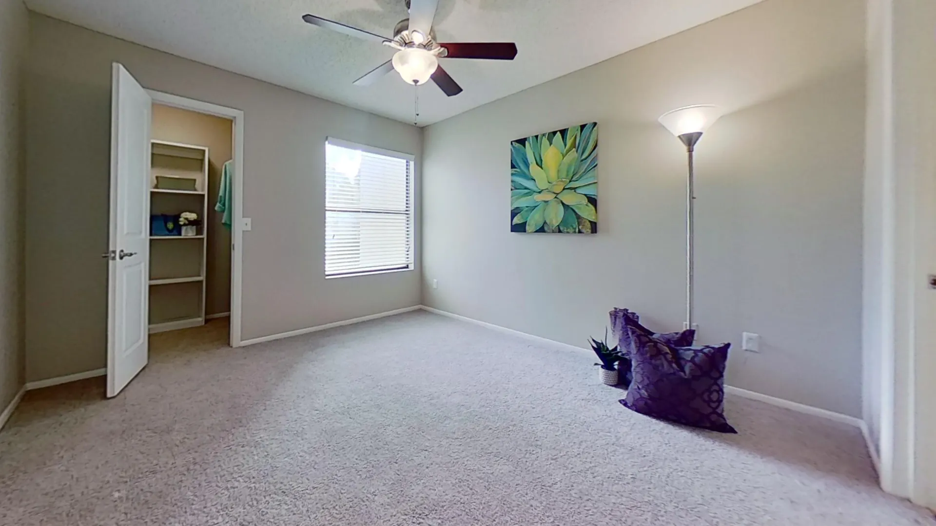 A spacious bedroom in the Martinique Autograph floor plan featuring a ceiling fan, carpeted flooring, a large window with natural light, and an open walk-in closet.