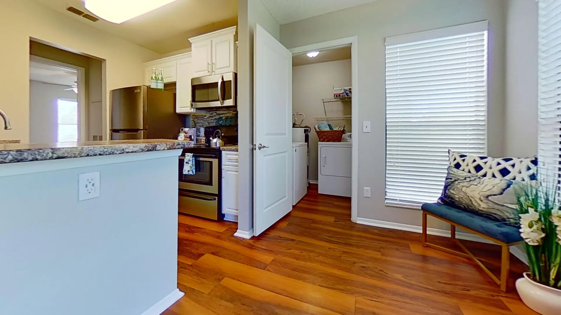 A view of the stylish kitchen in the Martinique Autograph floor plan, featuring stainless steel appliances, wood-style flooring, and an adjacent laundry room.