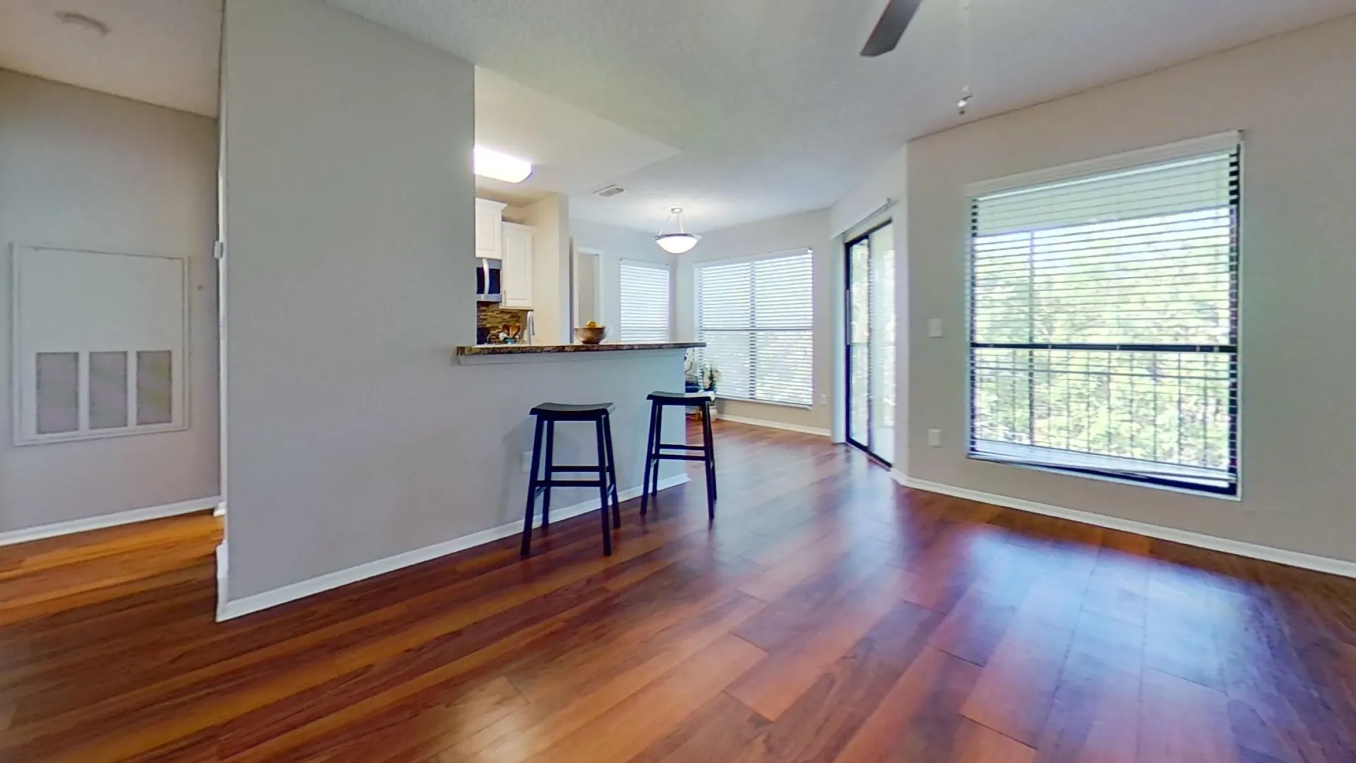 A bright and open living area in the Martinique Autograph floor plan, featuring wood-style flooring, large windows, a breakfast bar with seating, and access to a sunlit dining nook.