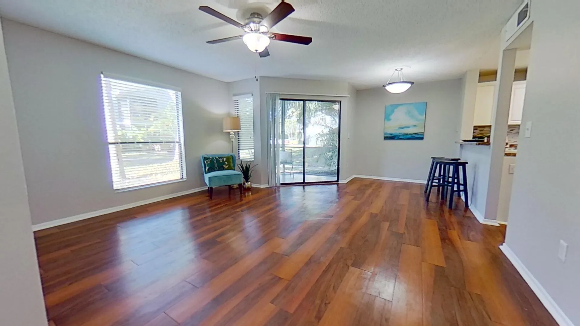 Living room with wood-style flooring, ceiling fan, and large windows in The Newport Autograph floor plan at River Reach Apartments.