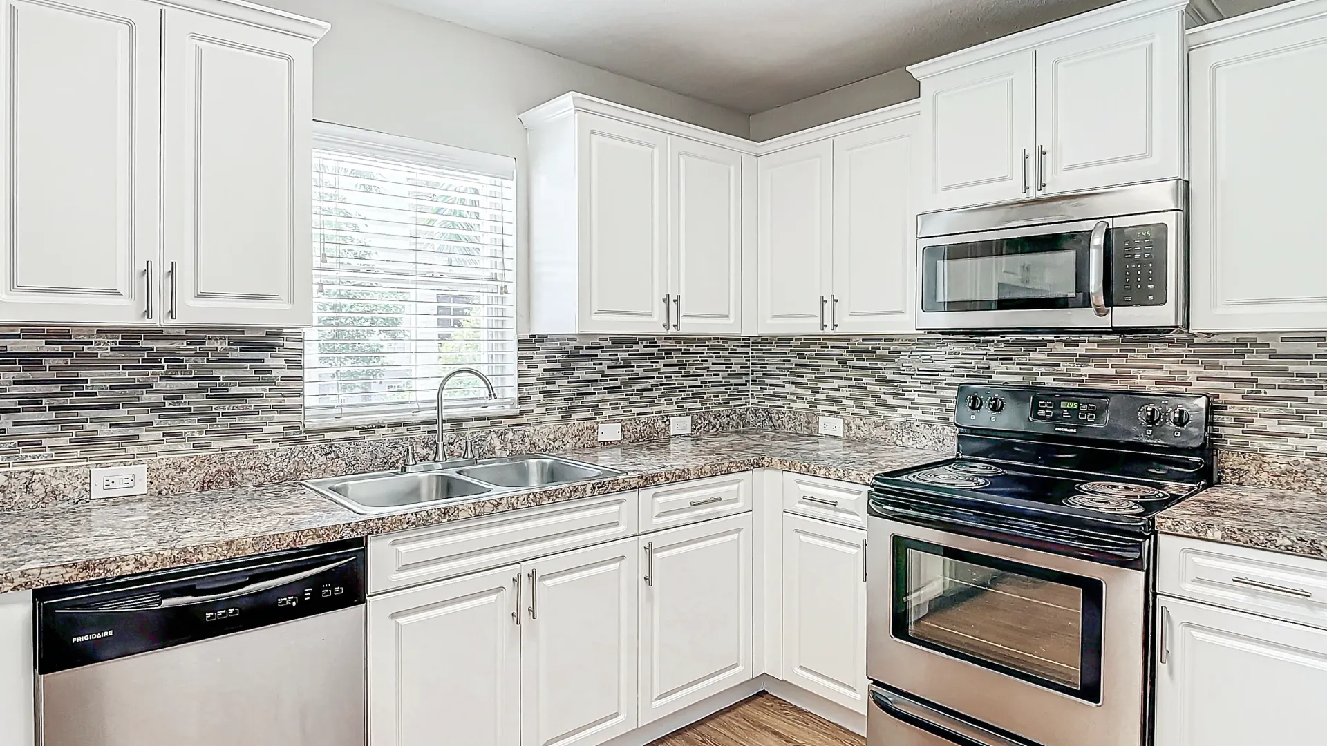 A stylish kitchen with stainless steel appliances, white cabinets, granite countertops, and a mosaic tile backsplash, providing a modern and elegant cooking space.