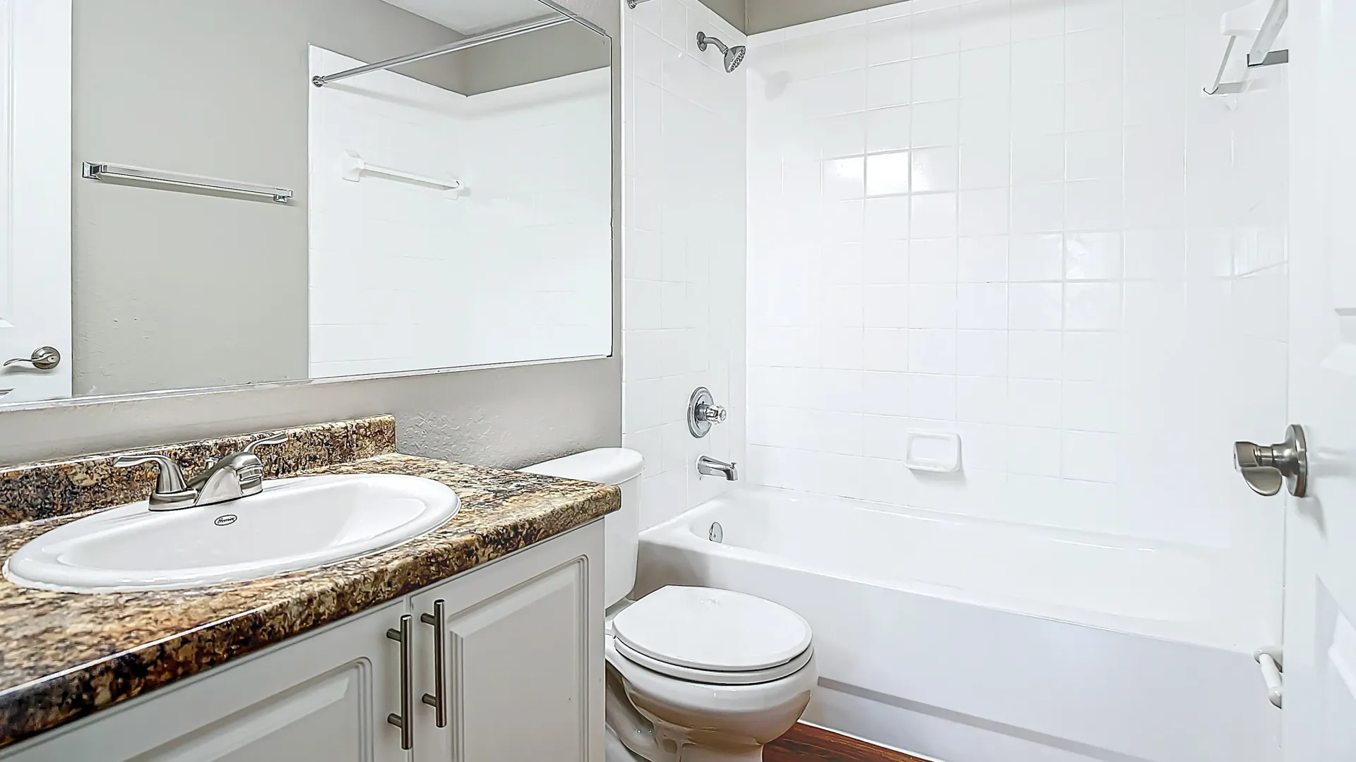 A modern bathroom with a granite-styl e countertop, white cabinetry, and a tiled shower and bathtub combo.