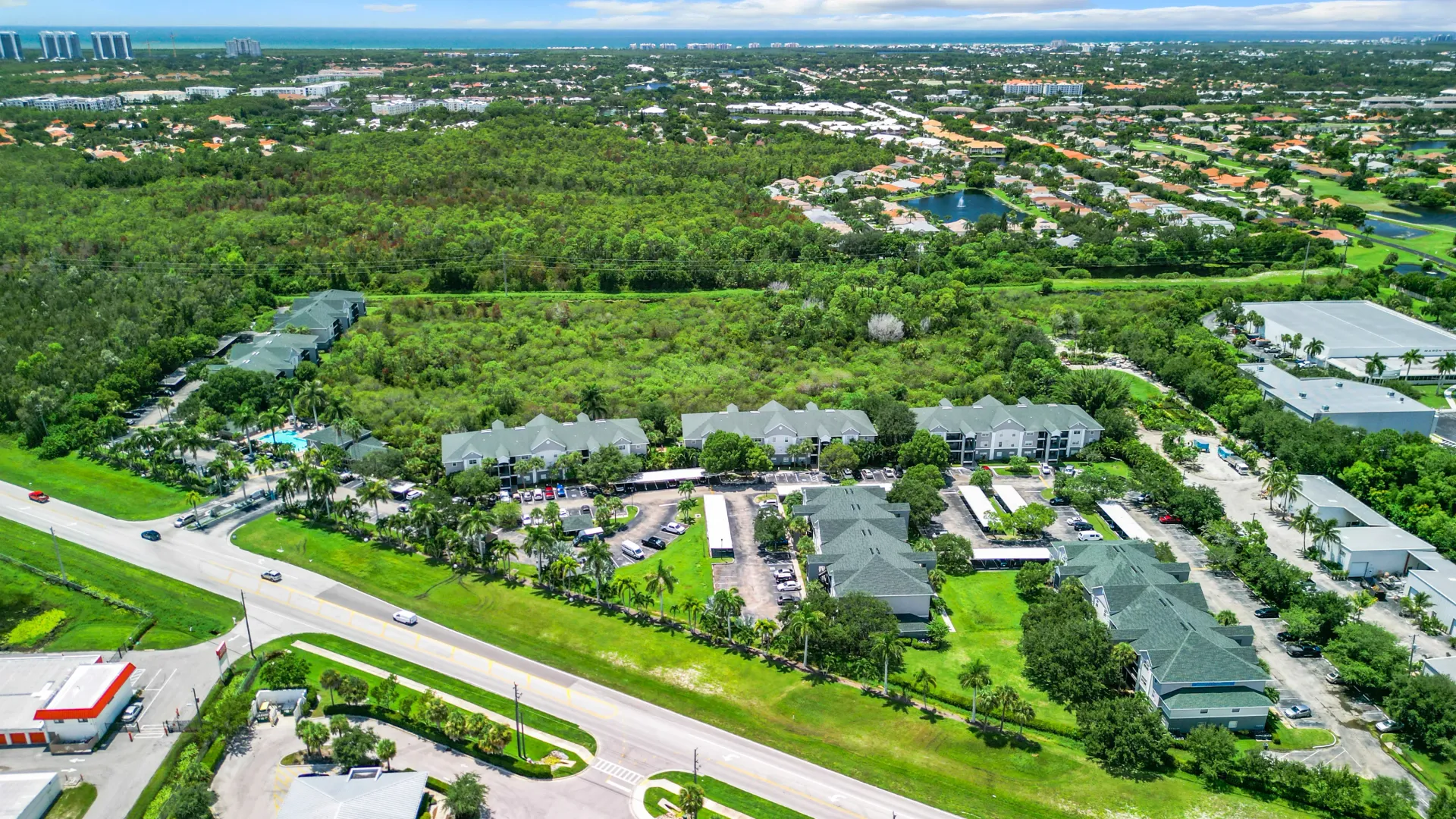 Aerial view of Somerset Palms Apartments surrounded by lush greenery, with residential buildings, parking areas, and nearby roads visible in the image.