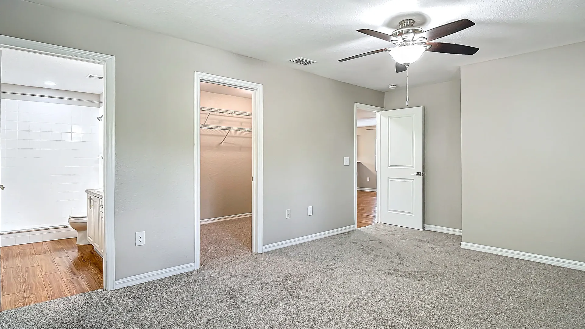 A bedroom with plush carpeting, ceiling fan, walk-in closet, and en-suite bathroom.