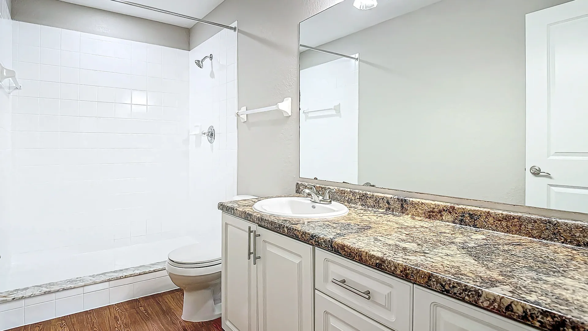 A bathroom with granite countertops, white cabinetry, and a walk-in shower.