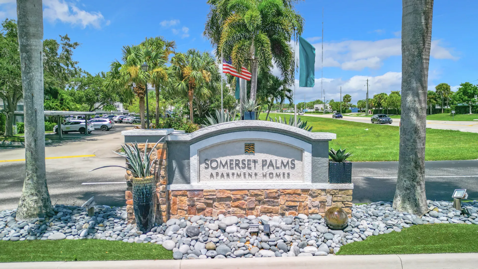 The entrance sign for Somerset Palms Apartment Homes, surrounded by palm trees and landscaped with stones and greenery.