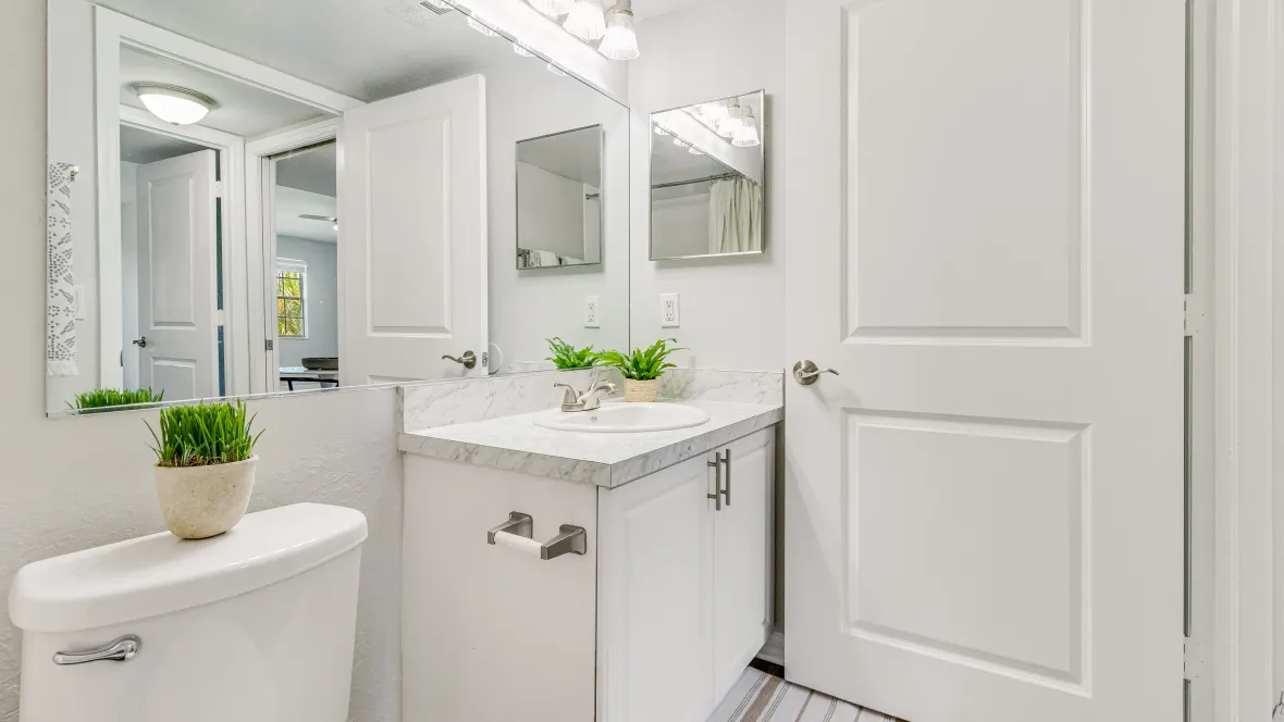 An impressive bathroom with wood-style flooring, a neutral granite-inspired vanity, a white tile shower/tub combo, and a large mirror
