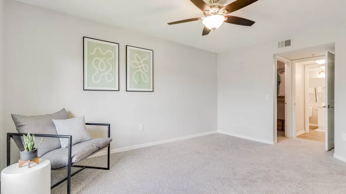 A welcoming master bedroom featuring soft carpeting, a brightly lit ceiling fan, and a glimpse into an impeccably organized walk-in closet 