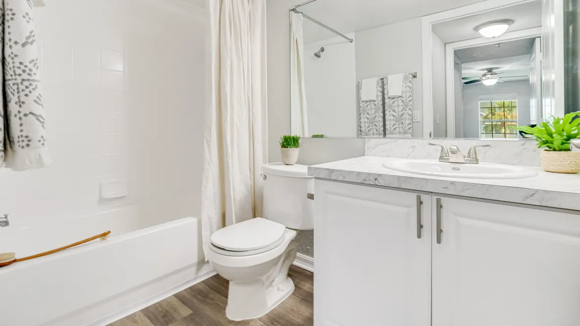 A sleek, modern bathroom adorned with wood-style flooring, white cabinetry, white Carrara countertops