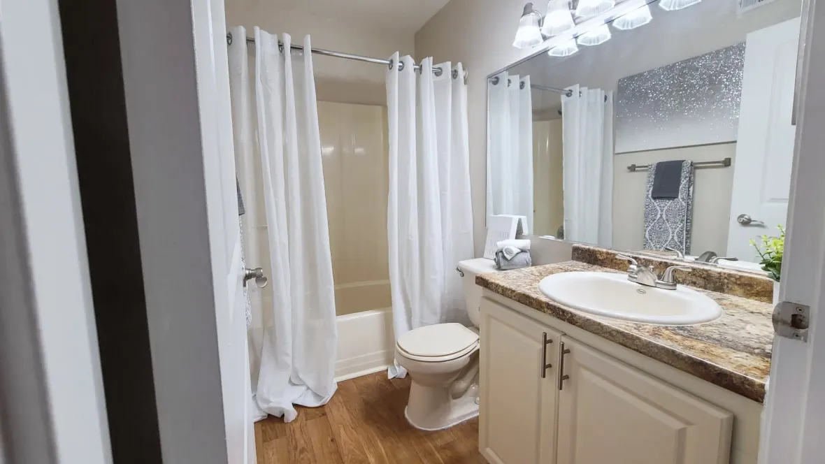 A generously sized bathroom, boasting an oversized mirror, bright overhead vanity lighting, and a shower/tub combo.