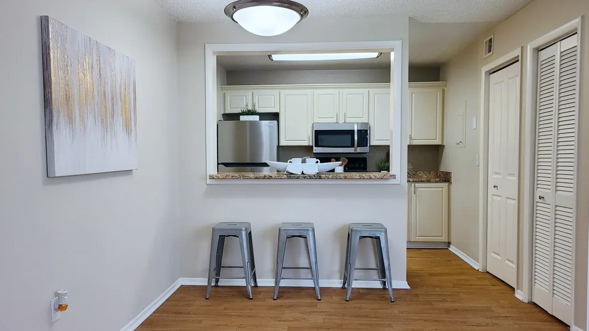 A kitchen that gracefully looks into the dining area – with an elegant light fixture and warm wood-like flooring. Breakfast bar offering counterspace overhang for more seating options.