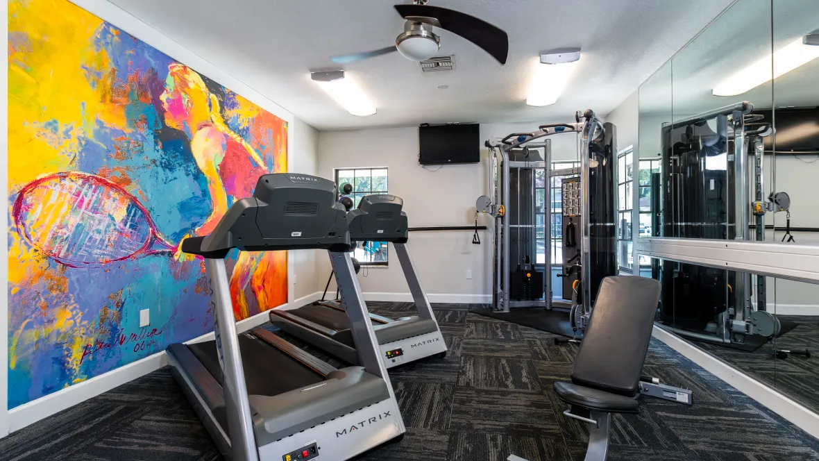 A vibrant fitness center, fully equipped with modern exercise equipment, featuring a lively mural depicting a girl playing tennis.