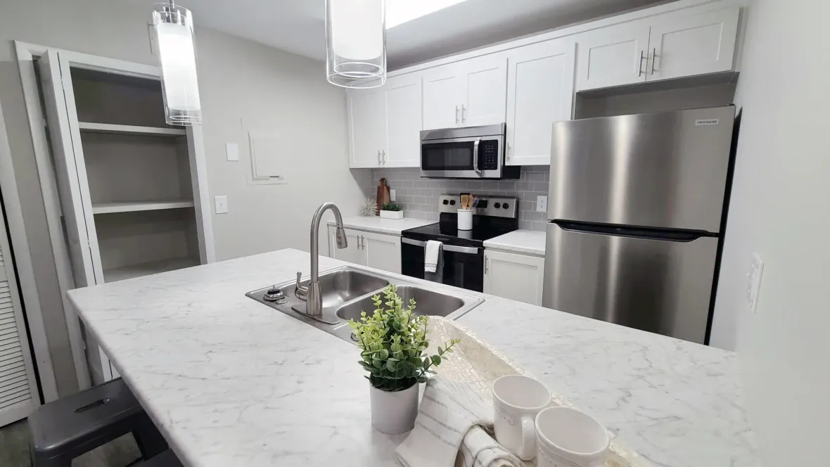 Elegant, spacious kitchen with modern white cabinetry, stylish grey tile backsplash, gleaming stainless steel appliances, and opulent marble-like countertops.