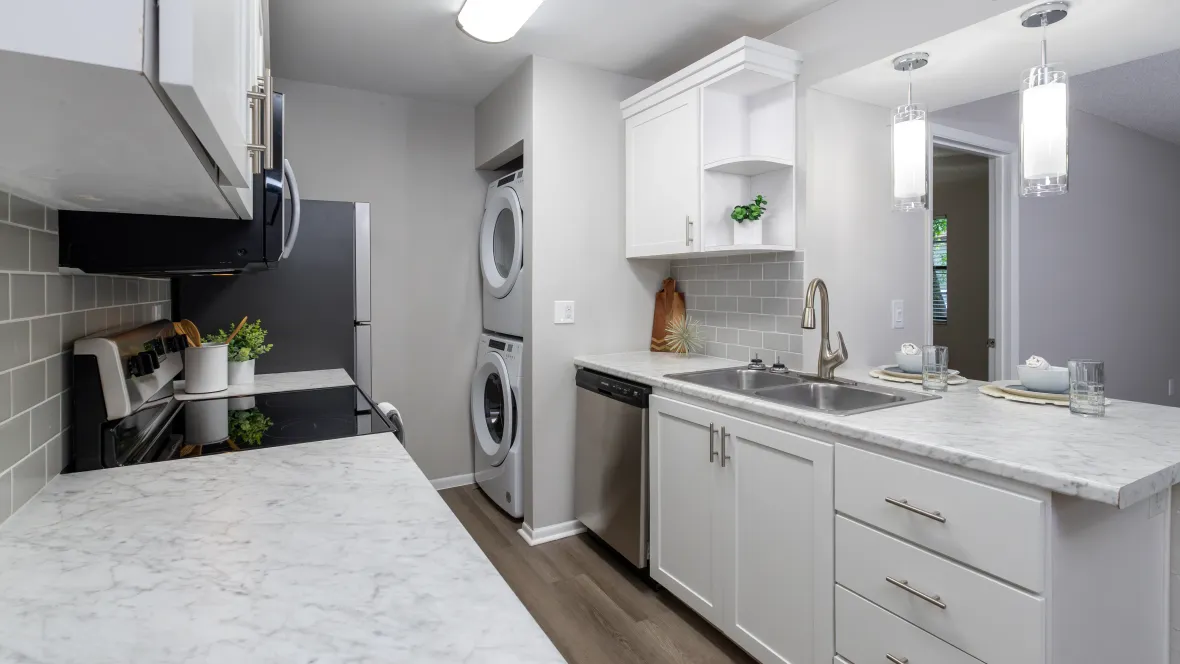 A galley-style kitchen boasting modern white cabinetry, a chic grey tile backsplash, stainless steel appliances, and luxurious countertops with a large breakfast bar and overhang for additional seating.