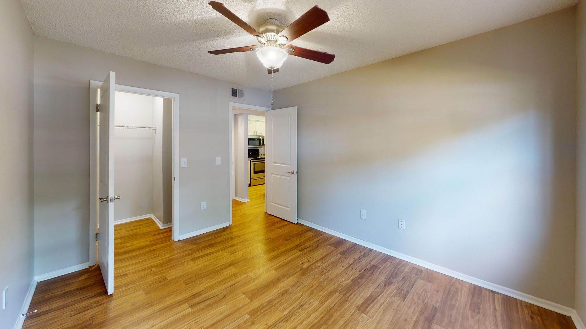 Bedroom in The Oakwood floor plan at Carrington Lane featuring wood-style flooring, ceiling fan, and a walk-in closet.