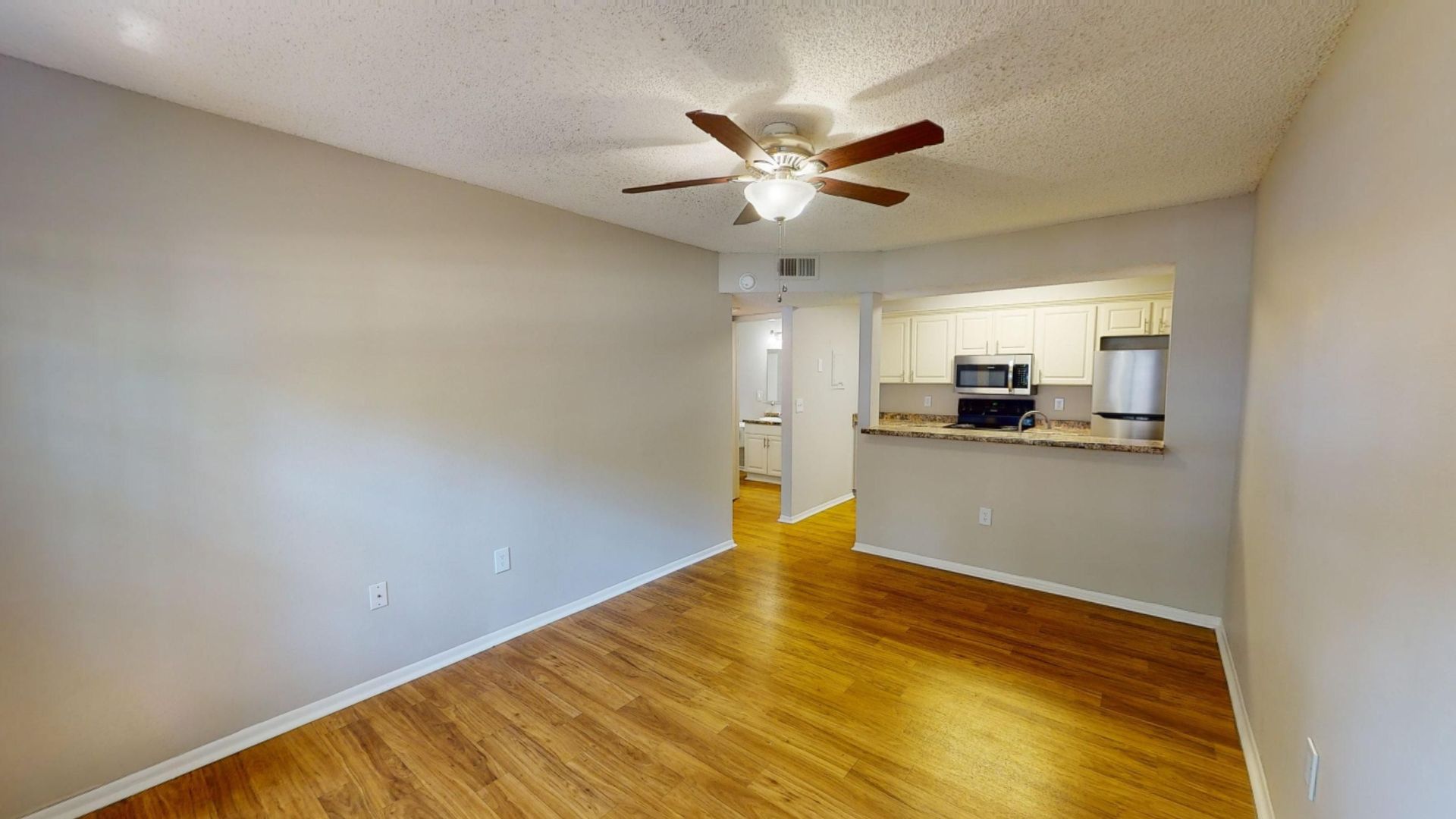 Living room in The Oakwood floor plan at Carrington Lane featuring wood-style flooring, a ceiling fan, and an open layout connected to the kitchen.