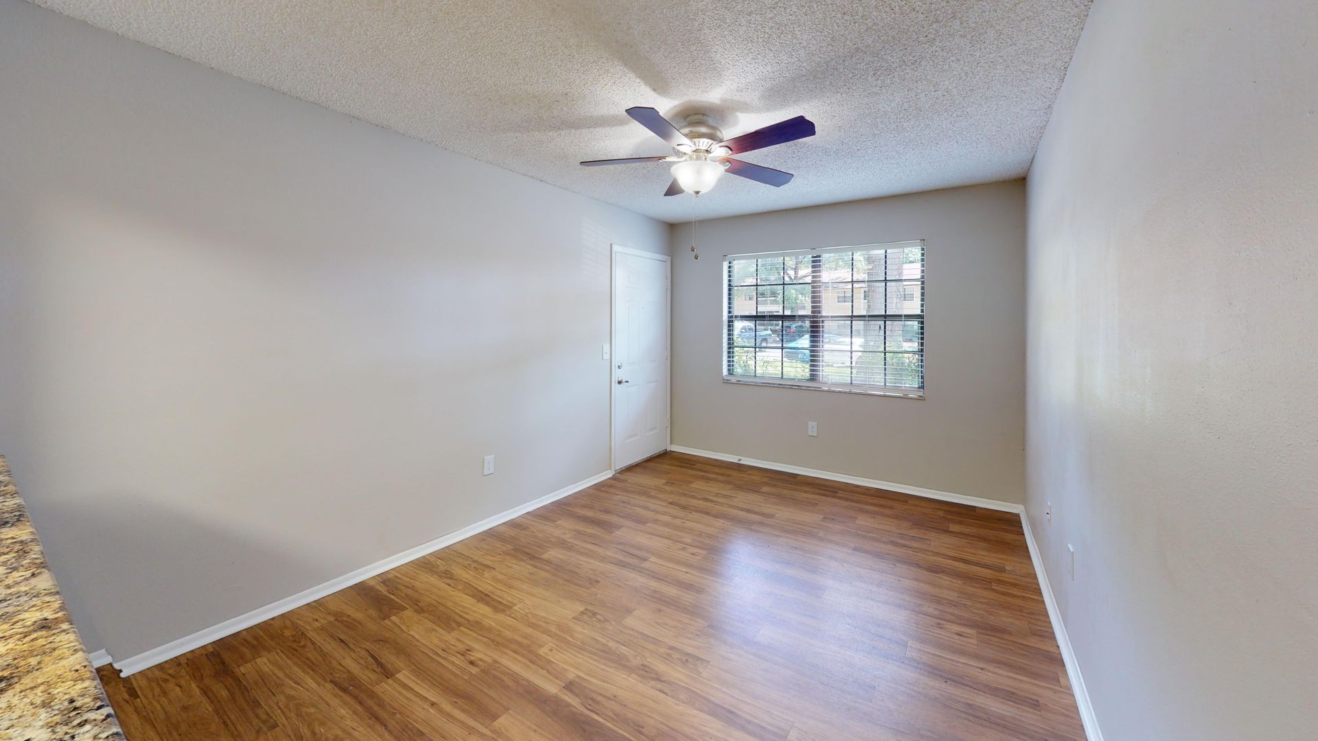 Living room in The Oakwood floor plan at Carrington Lane featuring wood-style flooring, a ceiling fan, large window, and spacious open layout.