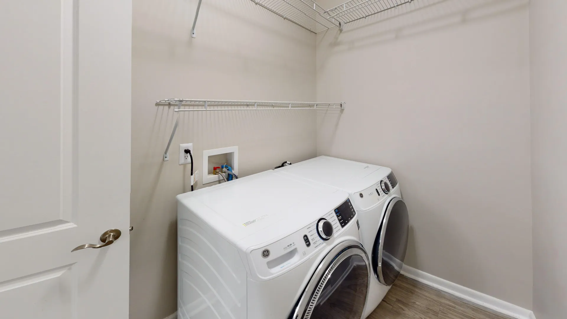 Laundry room in The Rosewood floor plan at Carrington Lane featuring a full-size washer and dryer, wood-style flooring, and built-in wire shelving.