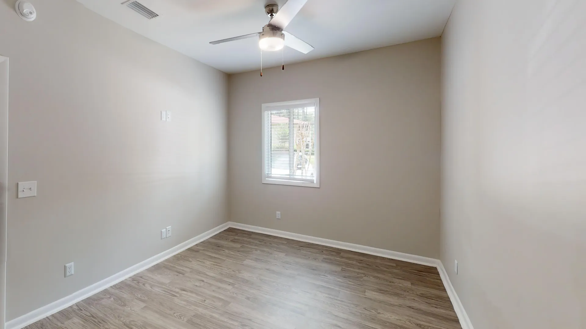 Bedroom in The Rosewood floor plan at Carrington Lane featuring wood-style flooring, a ceiling fan, neutral finishes, and a large window.