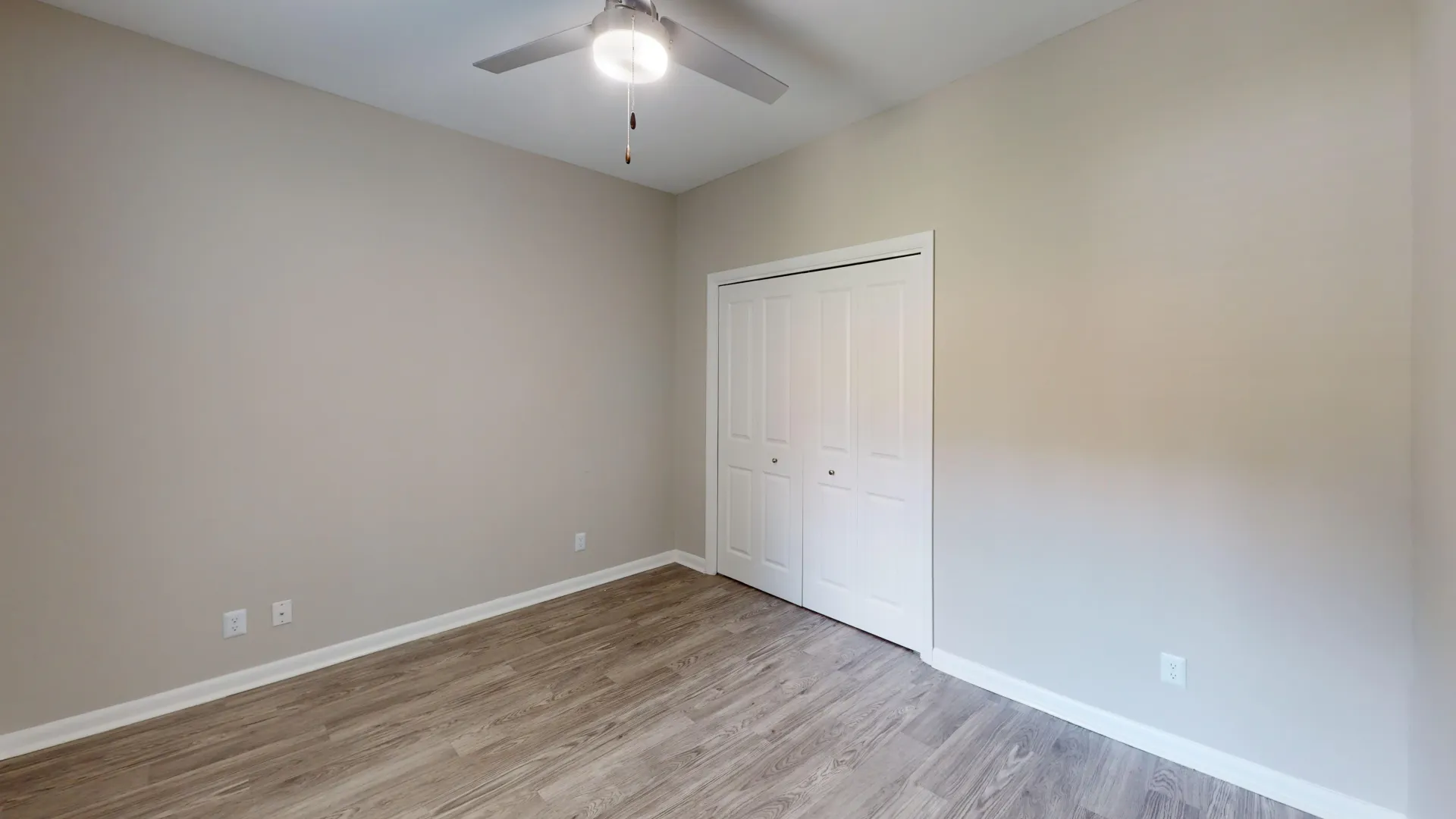 Spacious bedroom at Carrington Lane with wood-style flooring, modern ceiling fan, neutral finishes, and a double-door closet.