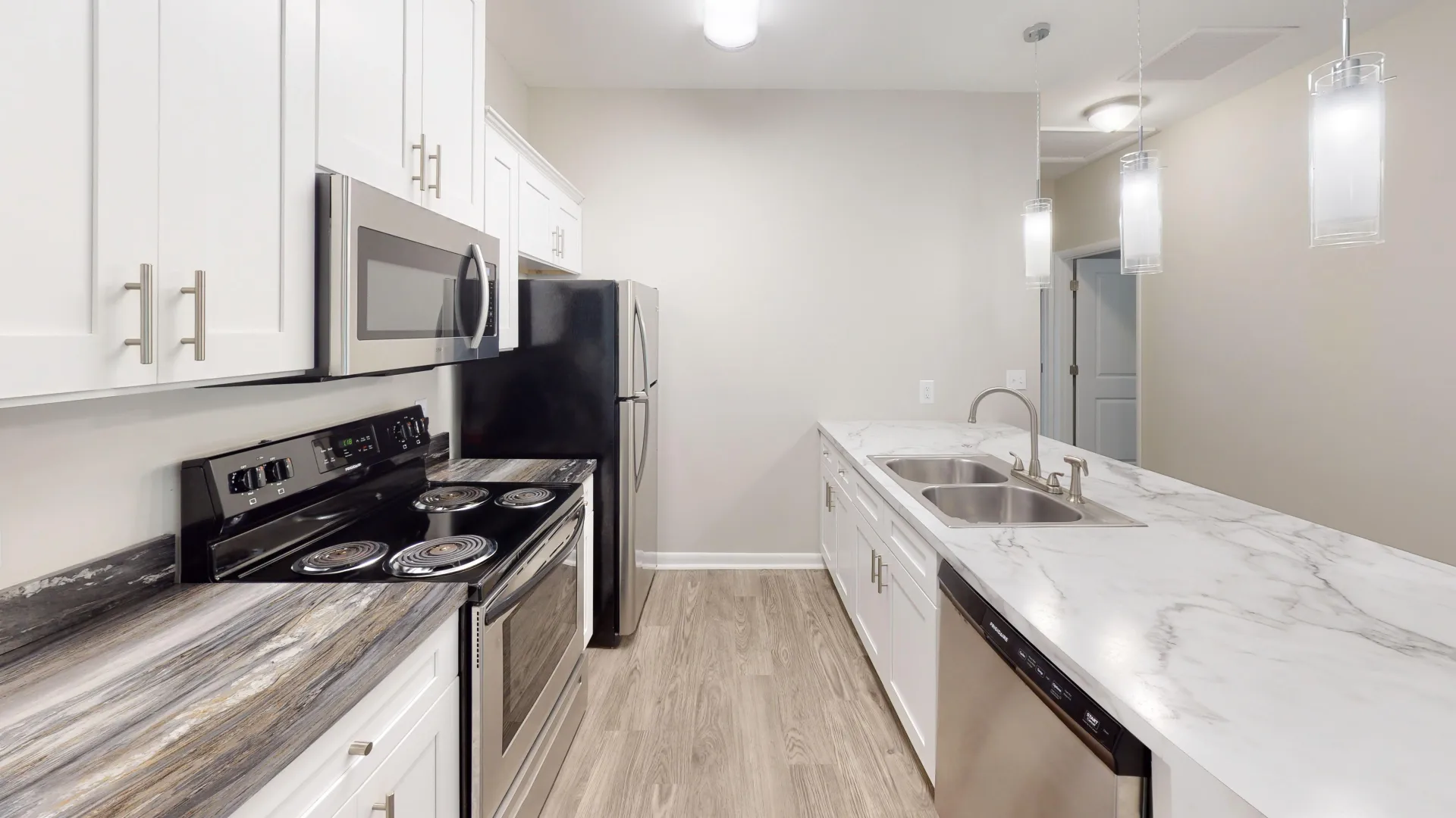 Kitchen in The Rosewood floor plan at Carrington Lane featuring a large center island, white cabinetry, stainless steel appliances, pendant lighting, and wood-style flooring.