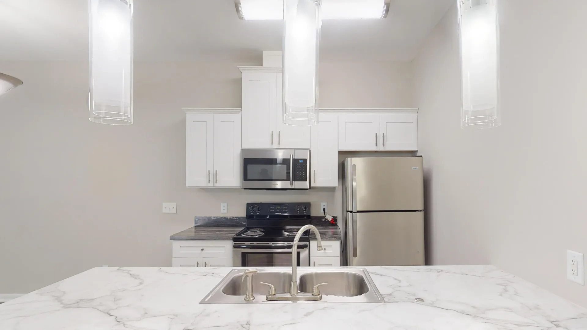 Kitchen in The Rosewood floor plan at Carrington Lane featuring stainless steel appliances, white cabinetry, a large island with sink, and pendant lighting.