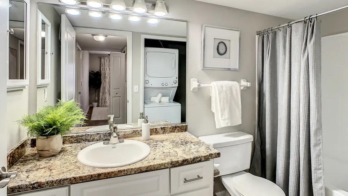 Bathroom with two white cabinets underneath sink and granite-style countertops, large mirror with vanity lighting, and garden tub.