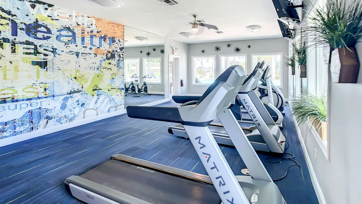 A fitness center with treadmills lined along the windows and televisions mounted to the walls.