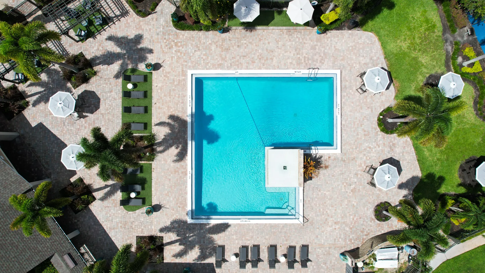 Aerial view of the resort-style pool at Harper Grand, showcasing lounging areas, umbrellas, and lush landscaping.