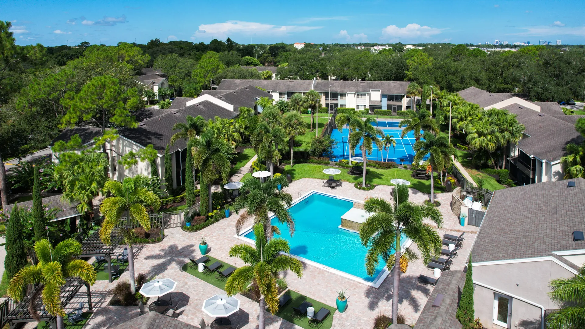 Aerial view of Harper Grand Apartments featuring a sparkling pool, lush landscaping, and a tennis court, showcasing the resort-style amenities available to residents.