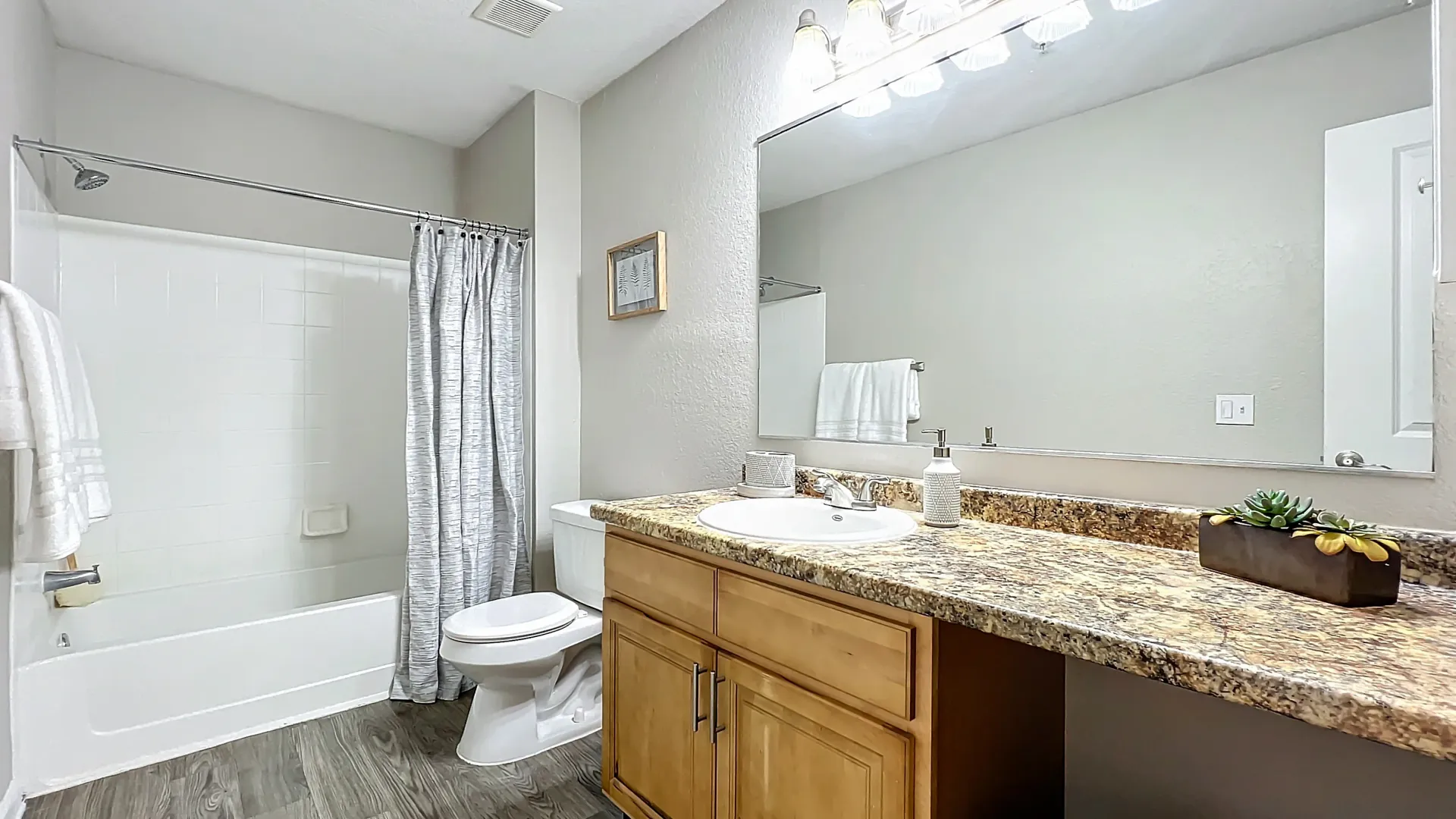 Modern bathroom with granite-style countertop, wooden cabinetry, and a shower-tub combo with a sleek curtain.