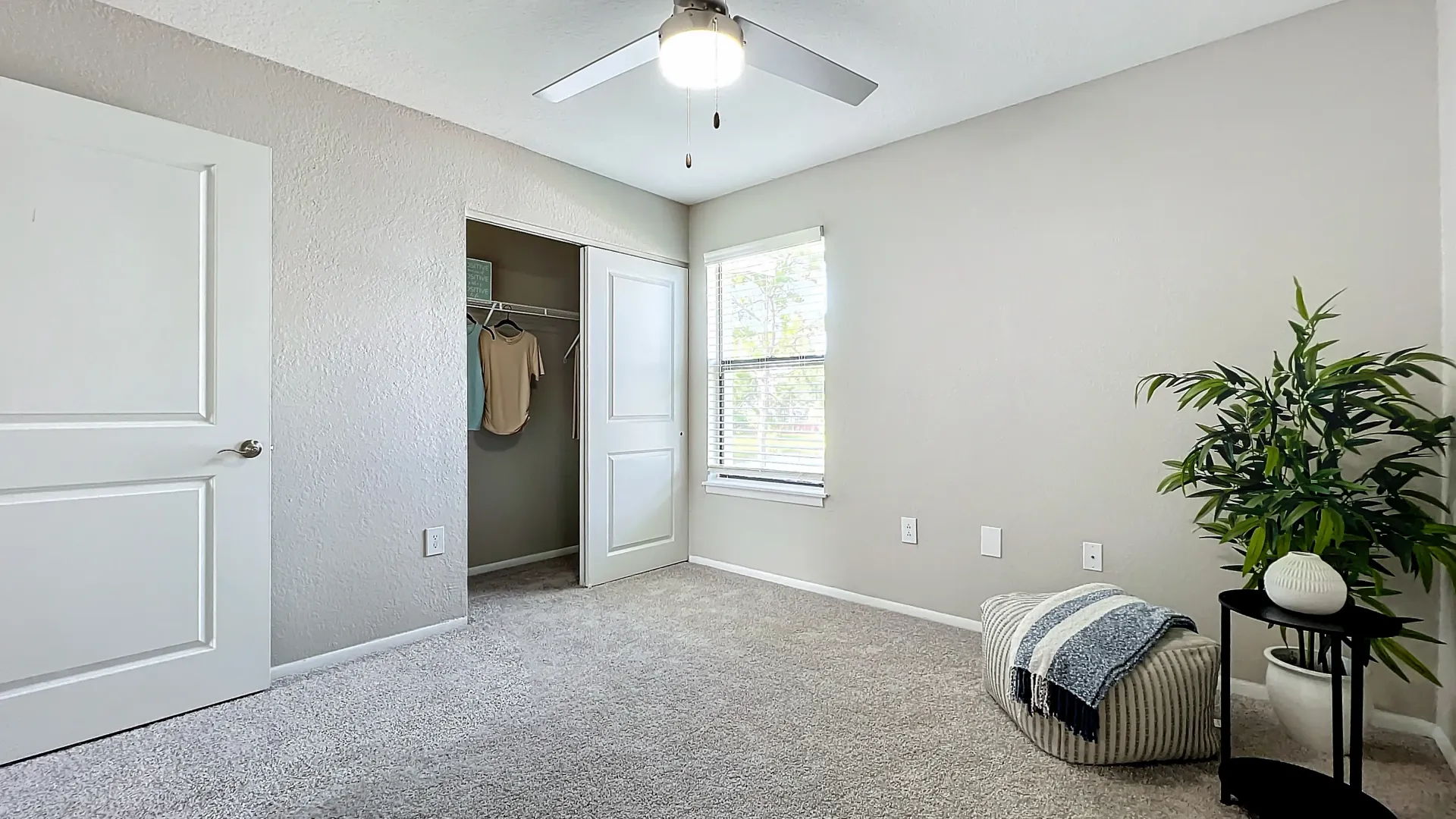 Spacious bedroom with plush carpeting, a large window, a ceiling fan, and an open closet.