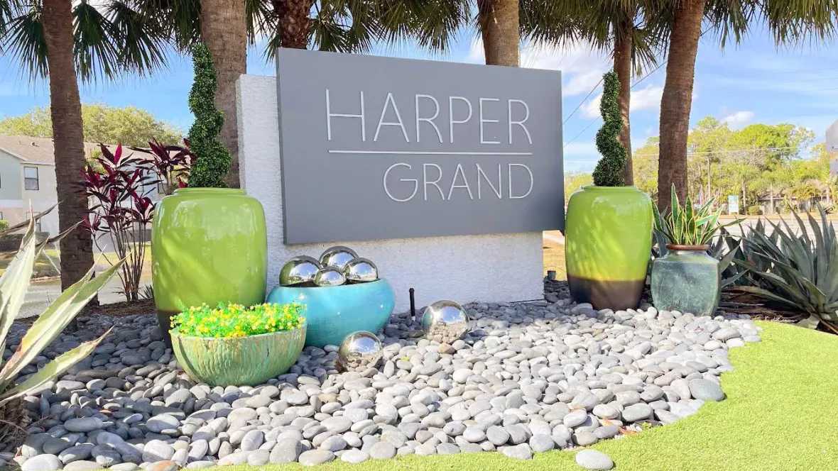 A grand entrance with monumental signage, framed by vibrant green planters and ornate metallic decorative balls, extending a warm welcome to residents and visitors alike.