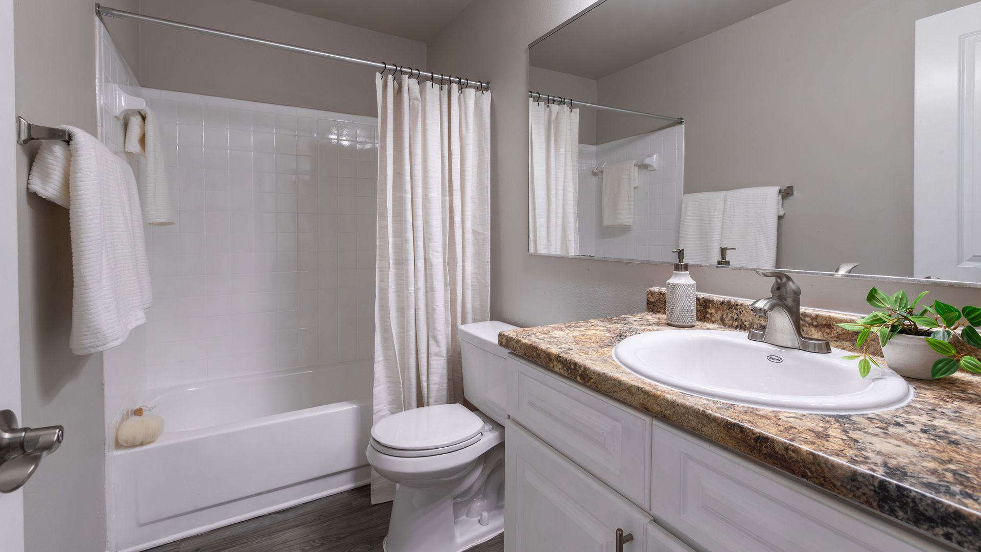 Bathroom with granite-inspired countertop, large mirror, and shower-tub combo at Harper Grand Apartments in Orlando, FL.